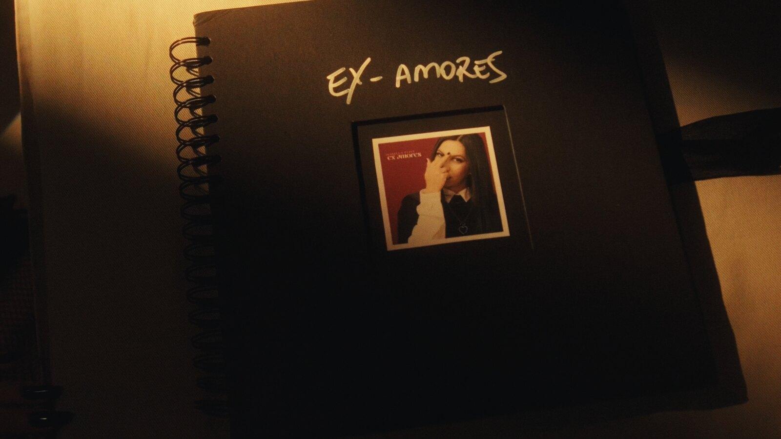Caderno preto com o título Ex-amores escrito à mão e a capa do single colada dentro, cena do clipe de Isabella Flint