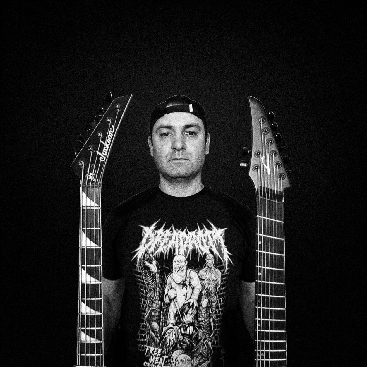 Erhan B, criador do Dreadrott, em foto preto e branco entre duas guitarras, vestindo camiseta da banda
