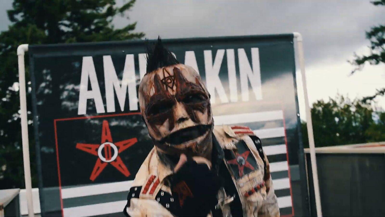 Integrante mascarado da Amerakin Overdose diante do painel com o nome da banda, em cena de clipe